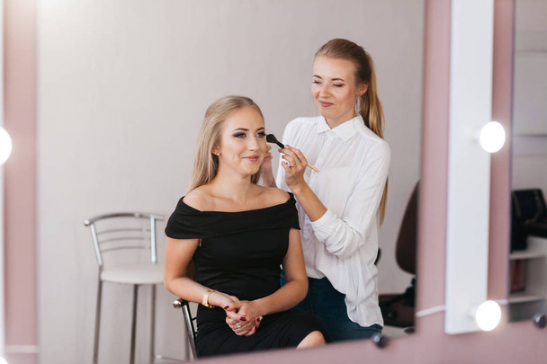 Artista de maquillaje profesional trabajando con una hermosa mujer joven en vestido negro
 - Foto, Imagen