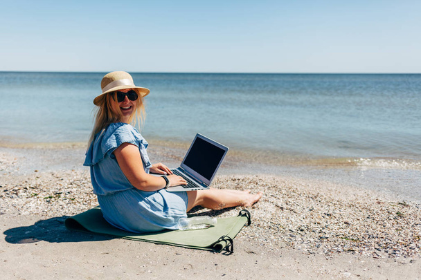 Laptop ile denize sıfır plaj üzerinde oturan genç güzel kadın - Fotoğraf, Görsel