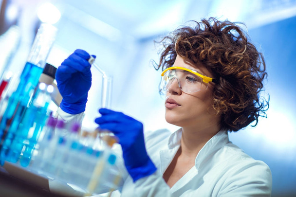 Young female scientist in protective glasses and gloves dropping - Photo, Image
