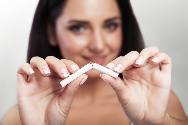Přestat kouřit. Closeup krásná šťastná žena lámání cigaretu. Portrét usmívající se žena držící cigaretu rozbité v rukou. Koncept zdravého životního stylu. - Fotografie, Obrázek