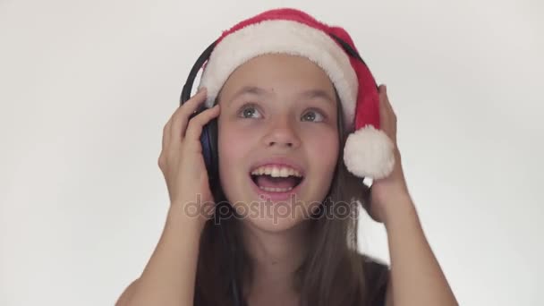Mooie Stout meisje tiener in een kerstman hoed luistert naar muziek op hoofdtelefoons en zingt langs op witte achtergrond stock footage video. - Video