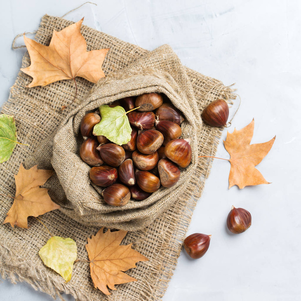 Herfst herfst oogst concept. Rijpe rauwe kastanjes in een doek zak op een gezellige keukentafel. Bovenaanzicht plat leggen - Foto, afbeelding