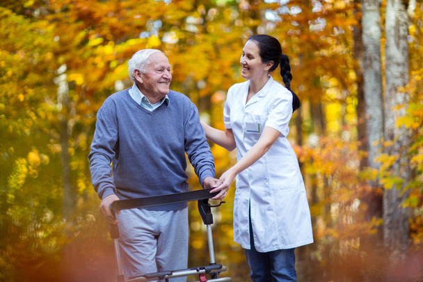 Медсестра помогает пожилому старику. Старший использует ходунки с
 - Фото, изображение