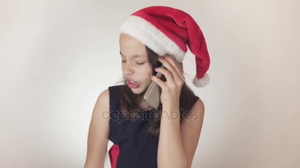 Mooie Stout meisje tiener in een kerstman hoed communiceert emotioneel op de smartphone op witte achtergrond stock footage video. - Video