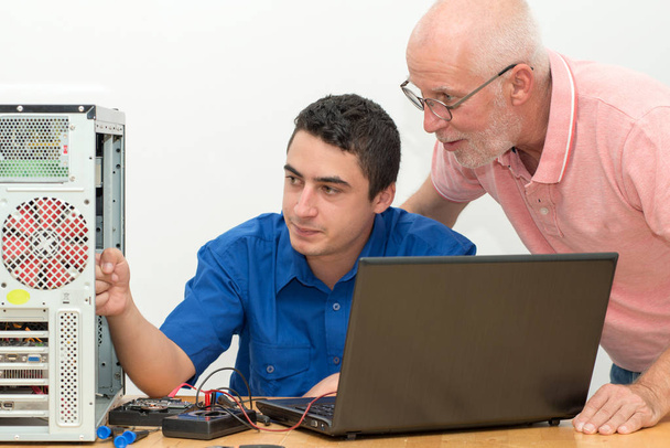 twee technici werken aan gebroken computer in werkplaats - Foto, afbeelding