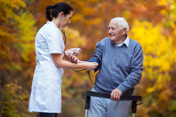 Enfermeira medir a pressão arterial do paciente velho ao ar livre
 - Foto, Imagem