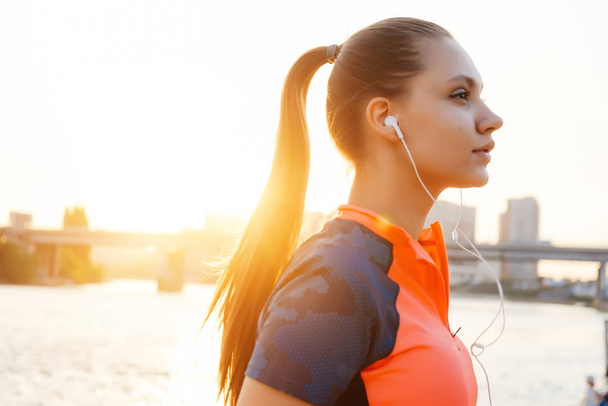 una hermosa joven corriendo por el río bajo el sol, escuchando música con auriculares
 - Foto, Imagen