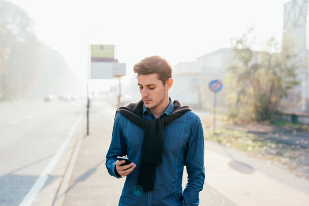jeune beau homme caucasien en plein air dans la ville contre-jour tenant téléphone intelligent technologie, réseau social, concept de communication
  - Photo, image