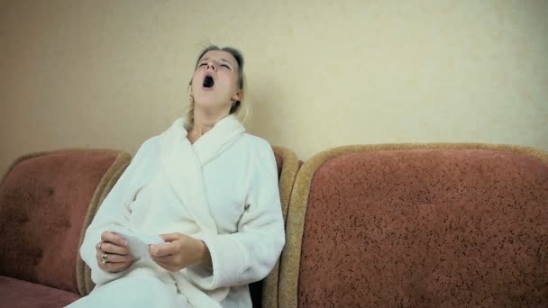 SLOW MOTION : jeune fille dans une robe de chambre à la maison éternue et essuie son nez avec un mouchoir sur le canapé
. - Séquence, vidéo