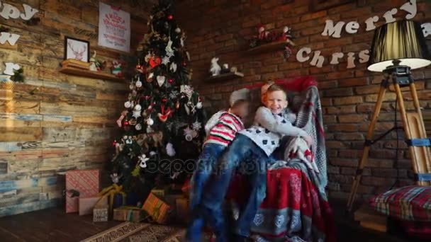 Irmãos nativos, meninos brincam e se divertem, pulam na poltrona grande no quarto com decorações de Natal
 - Filmagem, Vídeo