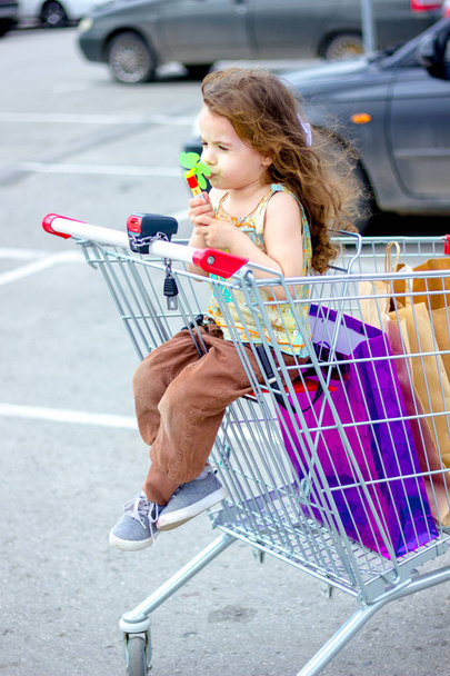 Little kid girl having fun sitting in a shopping trolley near the mall. - Foto, afbeelding