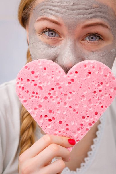 Woman having grey face mask holding heart sponge - Foto, Imagem