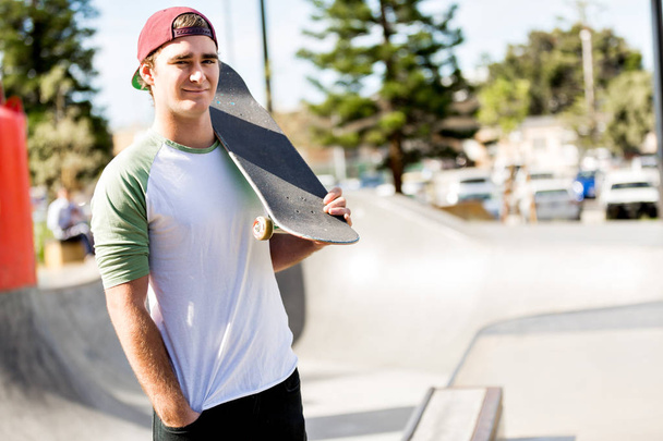 Teenage boy with skateboard standing outdoors - Valokuva, kuva