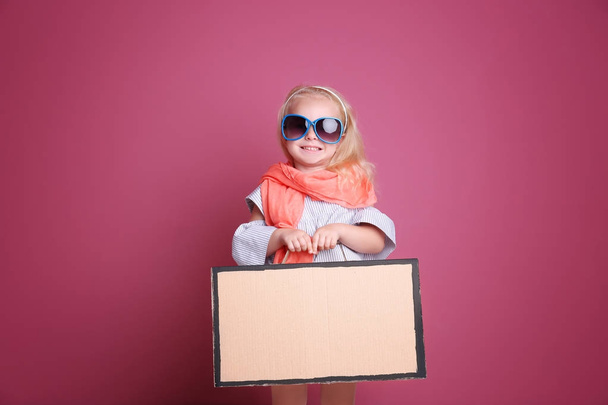 Little girl playing with cardboard suitcase on color background - 写真・画像