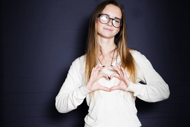 cute girl with glasses with long hair smiles and shows her hands with a heart, isolated on a blue background - Valokuva, kuva