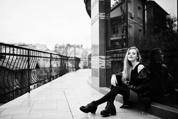 Blondes modisches Mädchen im langen schwarzen Ledermantel posierte gegen - Foto, Bild