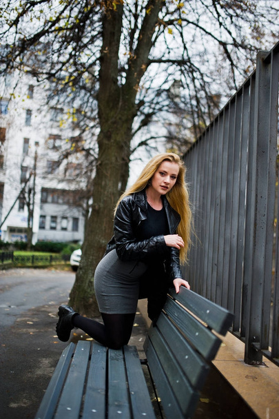 Blonde fashionable girl in long black leather coat posed on benc - Photo, image
