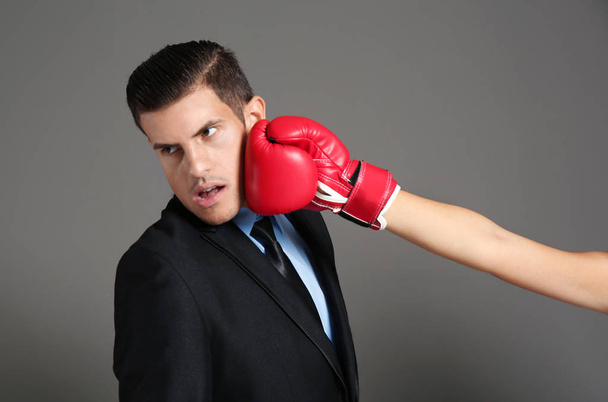 Hand of woman in boxing glove hitting businessman on grey background - Fotografie, Obrázek