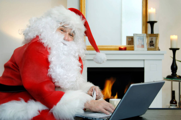 Santa Claus doing online shopping in his cozy Home, with a laptop and credit card - Foto, immagini