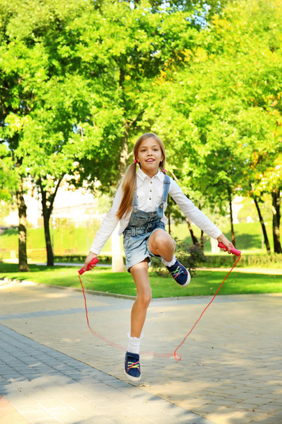 Cute little girl jumping rope in park - Фото, изображение