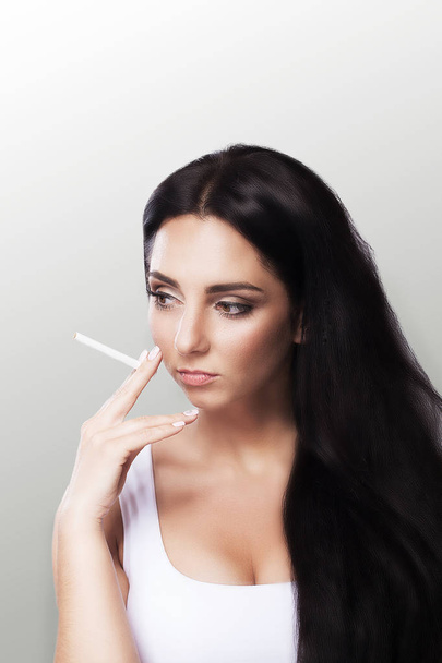 Smoke a young girl Beautiful young woman smoke a cigarette. Beautiful portrait. Girl with long black hair. The concept of health. On a gray background. - Foto, imagen