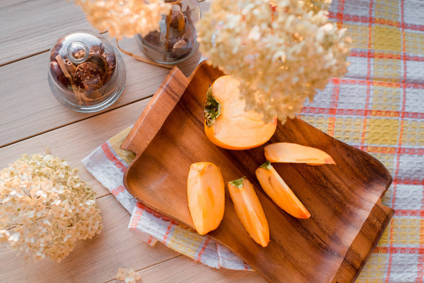 Autumn composition. Dried hydrangea, persimmon on a wooden tray on a yellow linen napkin - Fotó, kép