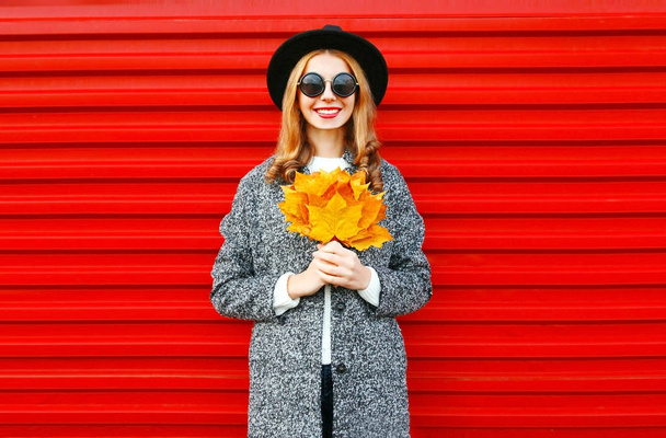 Fashion autumn smiling woman with yellow maple leaves on red bac - Photo, image