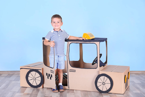 Little boy playing with cardboard taxi in light room - Zdjęcie, obraz