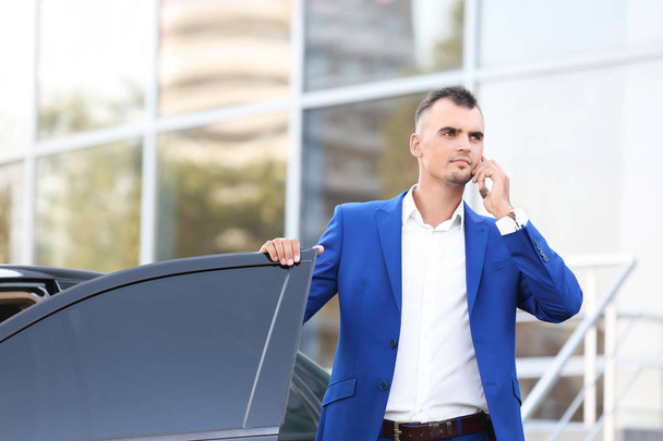 Young businessman talking on phone near car - Fotoğraf, Görsel