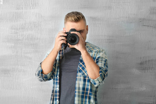 グレーの背景にカメラを持つ男性写真家 - 写真・画像