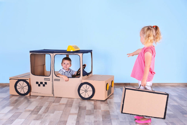 Little children playing with cardboard taxi in light room - Φωτογραφία, εικόνα