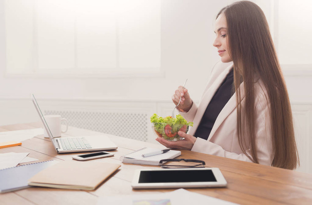 Giovane donna d'affari mangiare insalata in ufficio
 - Foto, immagini