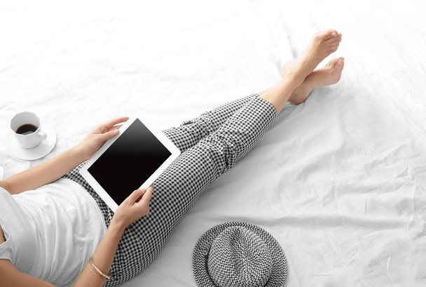 Young beautiful woman using tablet computer while sitting on bed - Foto, Imagem