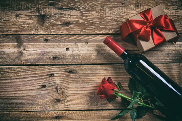 Valentines day. Red wine bottle, rose and a gift on wooden background - Photo, Image