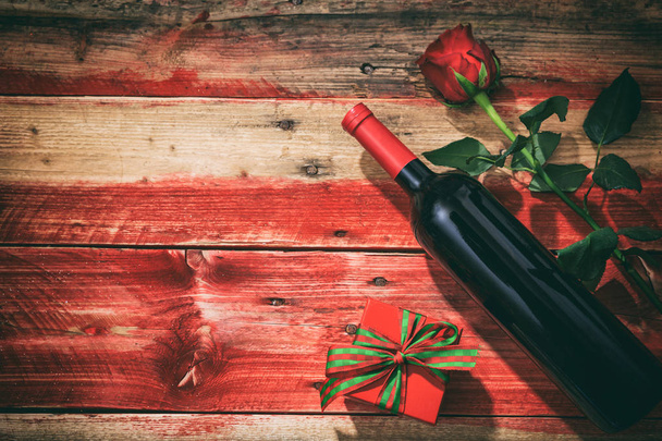 Sevgililer günü. Kırmızı şarap şişesi, gül ve ahşap arka plan üzerinde bir hediye - Fotoğraf, Görsel