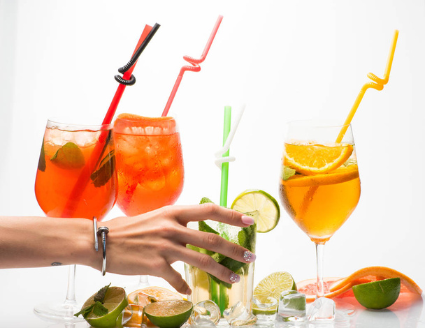 Drink and food. Alcoholic beverage and fruit at restaurant with hand of woman. Party and summer vacation. Fruit slice and cocktail glass at bar. Cocktails isolated on white background with mojito. - 写真・画像