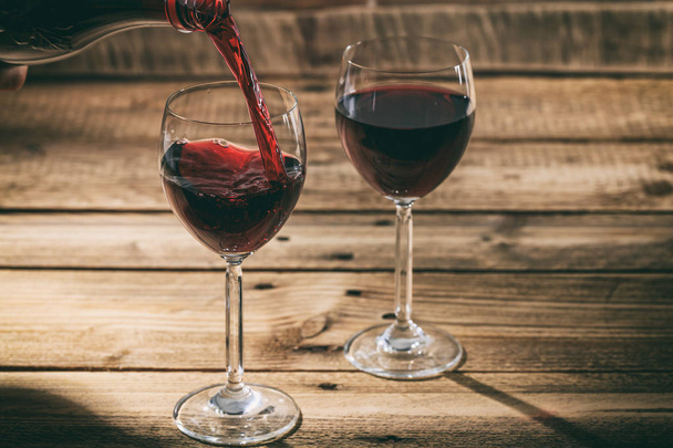Pouring red wine in a glass on wooden background - Fotografie, Obrázek