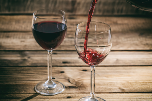 Wylewanie czerwonego wina w szklance na podłoże drewniane - Zdjęcie, obraz