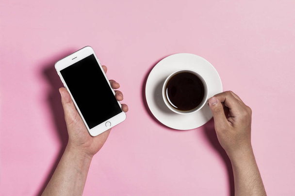 κρατώντας το κύπελλο καφέ και τηλέφωνο σε ροζ φόντο. - Φωτογραφία, εικόνα