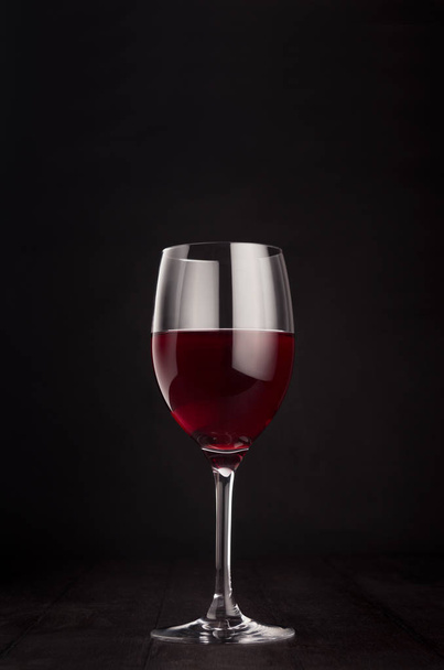 Wine glass with red wine on elegant dark black wooden background, copy space, vertical.  - Фото, изображение