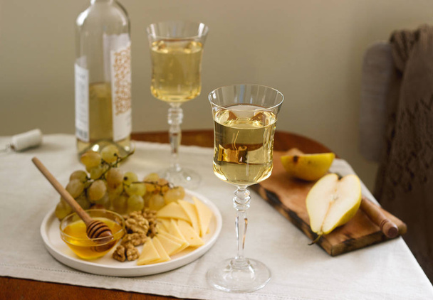 Okulary z białego wina i butelkę wina z przekąskami - ser, orzechy włoskie i winogron. Styl rustykalny. - Zdjęcie, obraz