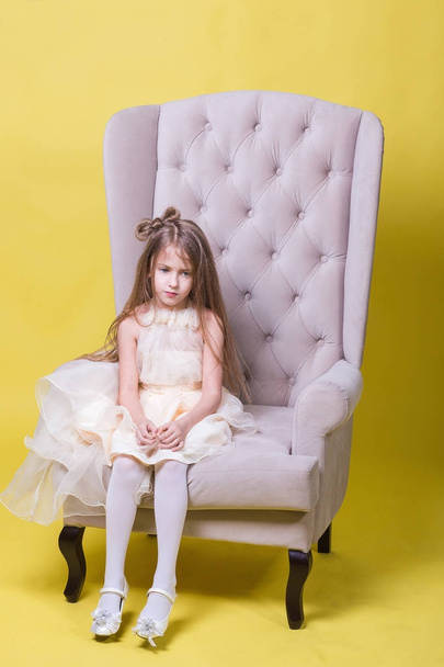 Teenager girl in a dress on a yellow background posing for the camera and sits on the chair - Fotoğraf, Görsel