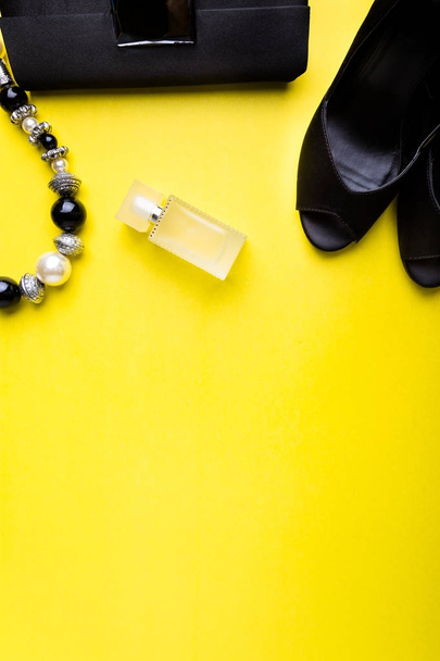 Damenmode Accessoires Set. Schwarz-Gelb. Minimal. schwarze Schuhe, Armband, Parfüm und Tasche auf gelbem Hintergrund. flache Lage. - Foto, Bild