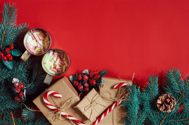 Fir branch, gift box and two cups of cocoa with marshmallows on red background - Foto, imagen