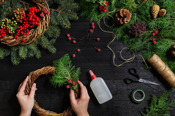 Pohled shora na ženské ruce vyrobit vánoční věnec. Balení dárků a svitky, smrkové větve a nástroje na dřevěný stůl. - Fotografie, Obrázek