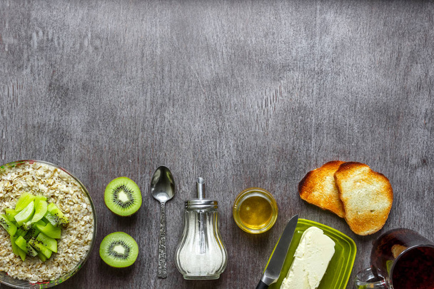 Havermout met kiwi, toast met boter en honing op een houten tafel. Het concept van een gezond ontbijt - Foto, afbeelding