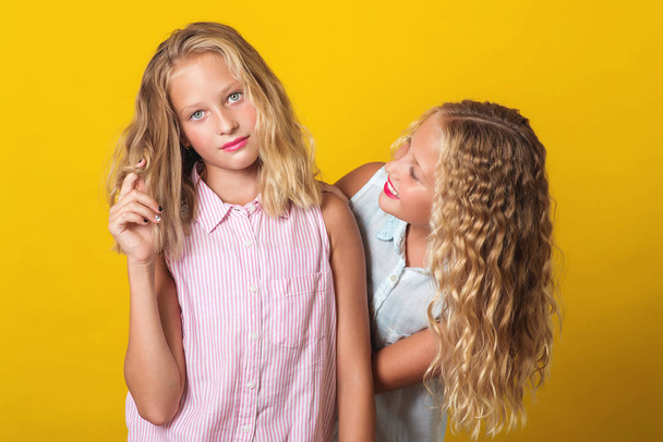 Funny girls twins have fun together on yellow background. - Zdjęcie, obraz