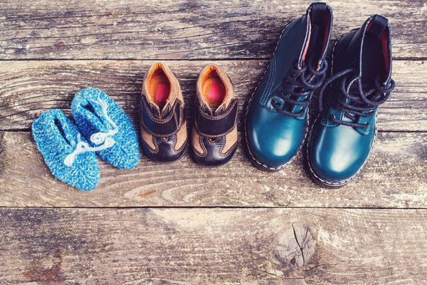 Zapatos para niños diferentes sobre fondo de madera oscura. Zapatos de punto de bebé y botas de cuero para niños para clima frío
. - Foto, Imagen