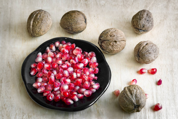 Pomegranate fruits on the plate and walnuts. - Photo, Image