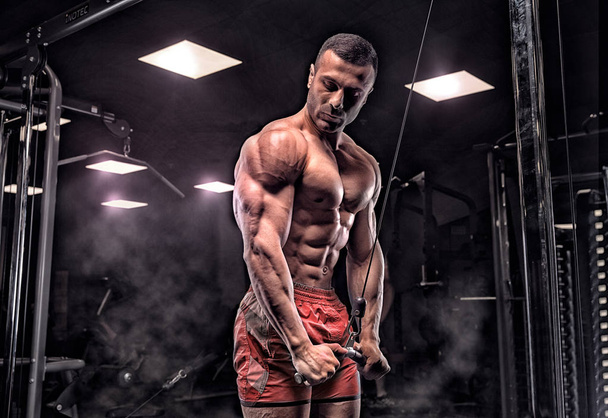 man in gym. Muscular bodybuilder guy doing exercises with barbel - Fotó, kép